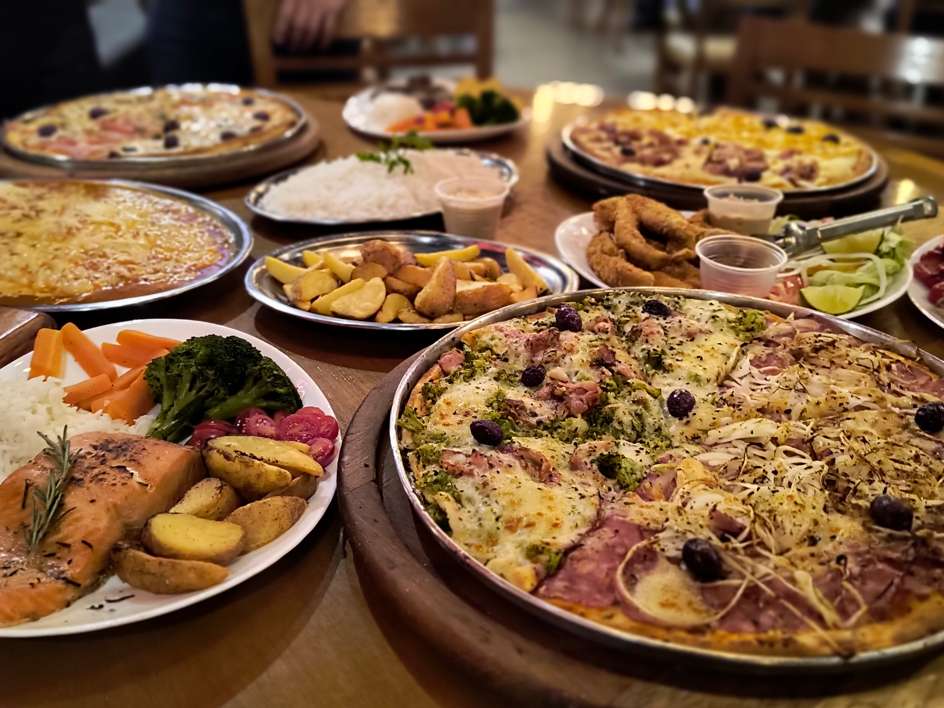 Mesa farta com variedade de pratos da Pizzaria Monções